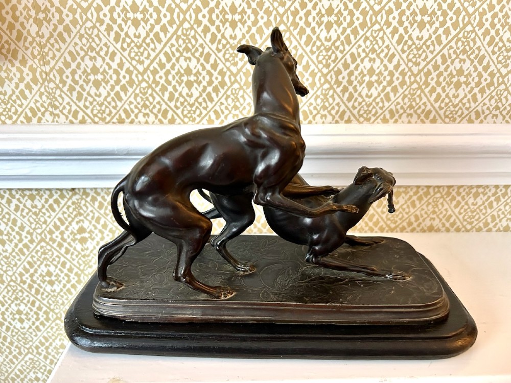 A dark brown patinated spelter sculpture depicting two whippets on a detailed relief base mounted upon a moulded wooden plinth. View II
