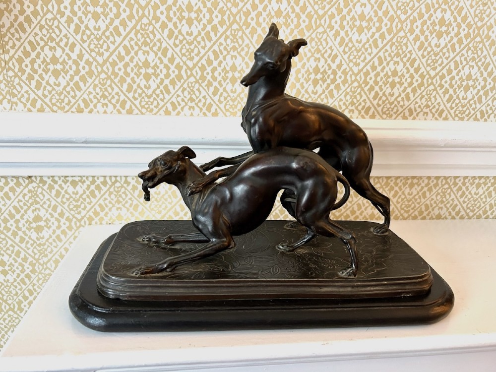 A dark brown patinated spelter sculpture depicting two whippets on a detailed relief base mounted upon a moulded wooden plinth. View III