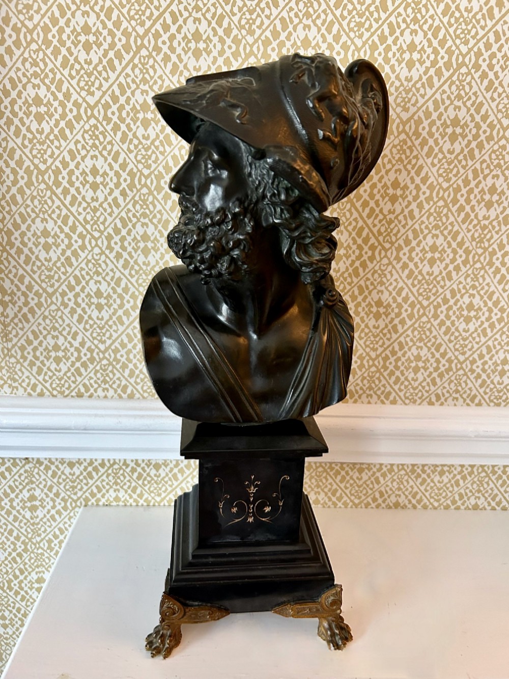 A 19th-century dark bronze bust depicting the classical figure Ajax wearing a crested helmet, mounted on a black marble pedestal with gilt feet.