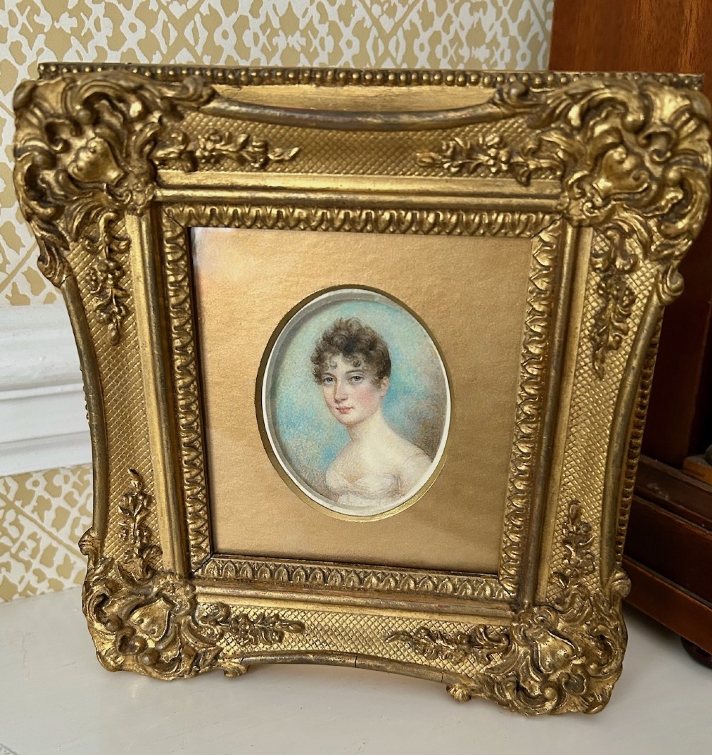 An early nineteenth-century oval watercolour portrait miniature of a lady in a white gown set within a rectangular carved giltwood frame. View II