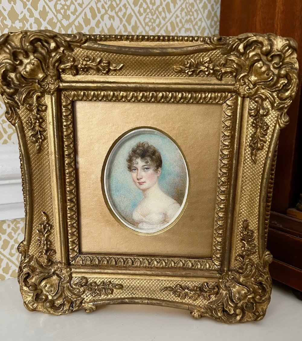 An early nineteenth-century oval watercolour portrait miniature of a lady in a white gown set within a rectangular carved giltwood frame. View III