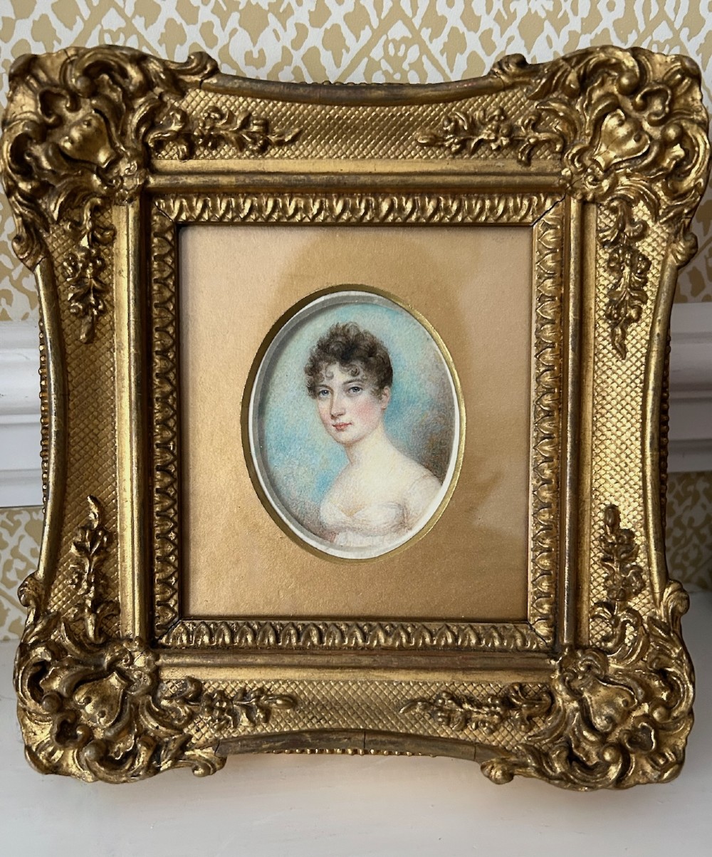 An early nineteenth-century oval watercolour portrait miniature of a lady in a white gown set within a rectangular carved giltwood frame. View V