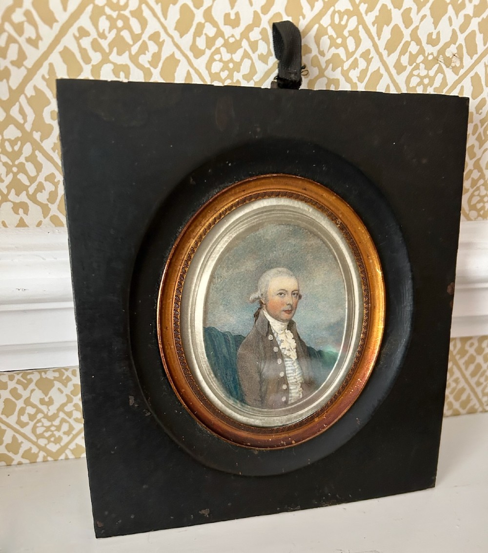 An antique oval watercolour portrait miniature painting of a gentleman wearing a brown coat and wig, housed in a square ebonised frame with a gilt inner slip and hanging loop. View IV