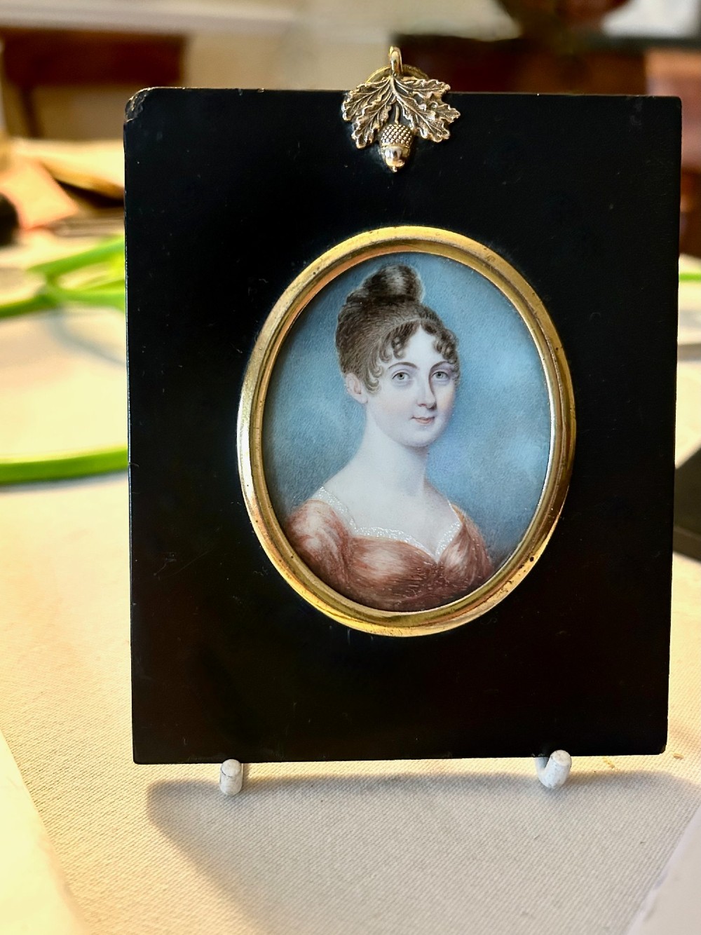 A late 18th-century oval portrait miniature depicting a lady in a red dress, mounted in an ebonised frame with a gilt brass bezel and acorn hanger.