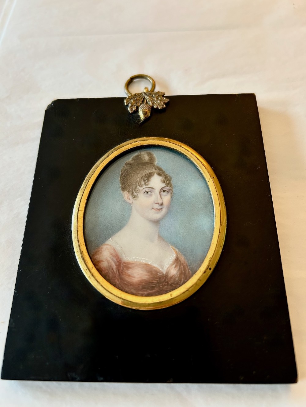 A late 18th-century oval portrait miniature depicting a lady in a red dress, mounted in an ebonised frame with a gilt brass bezel and acorn hanger. View II