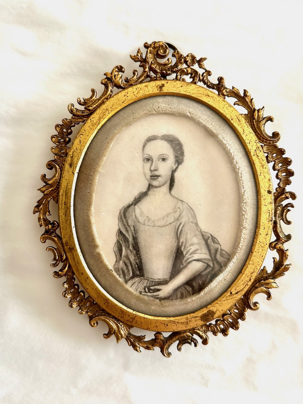 An 18th-century monochrome oval portrait miniature of a lady wearing Georgian dress, set within an ornate carved gilt frame.