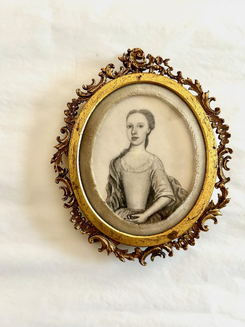An 18th-century monochrome oval portrait miniature of a lady wearing Georgian dress, set within an ornate carved gilt frame. View V
