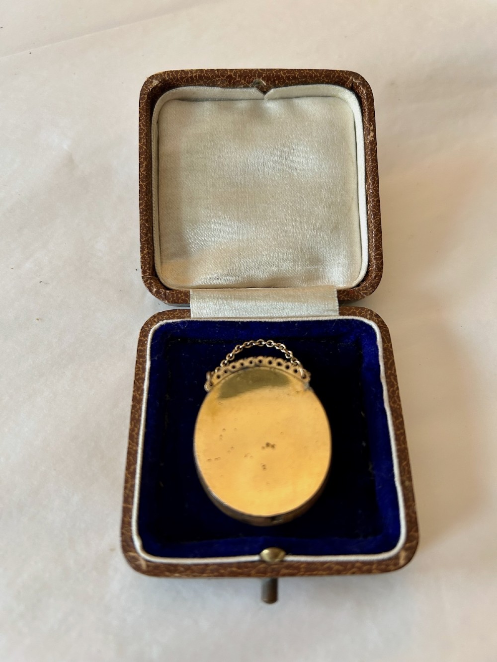 An oval late 18th-century portrait miniature depicting a young boy with light brown hair, set in a gold frame with a chain inside a velvet-lined leather presentation case. View II
