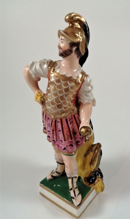 fig 1. An antique hand-painted porcelain figure depicting the Roman god Mars in gilded armour, a pink tunic, and a golden helmet, standing on a green base.