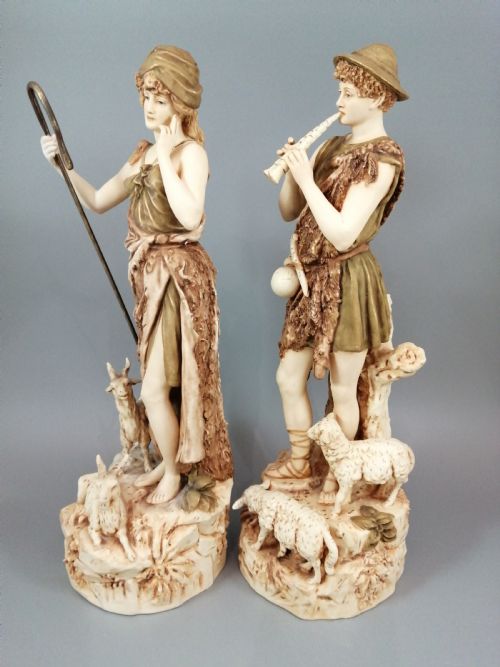 fig 1. A pair of antique Royal Dux porcelain statuettes depicting a shepherdess holding a staff beside goats and a shepherd playing a pipe beside sheep.