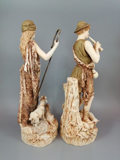 fig 4. A pair of antique Royal Dux porcelain statuettes depicting a shepherdess holding a staff beside goats and a shepherd playing a pipe beside sheep.