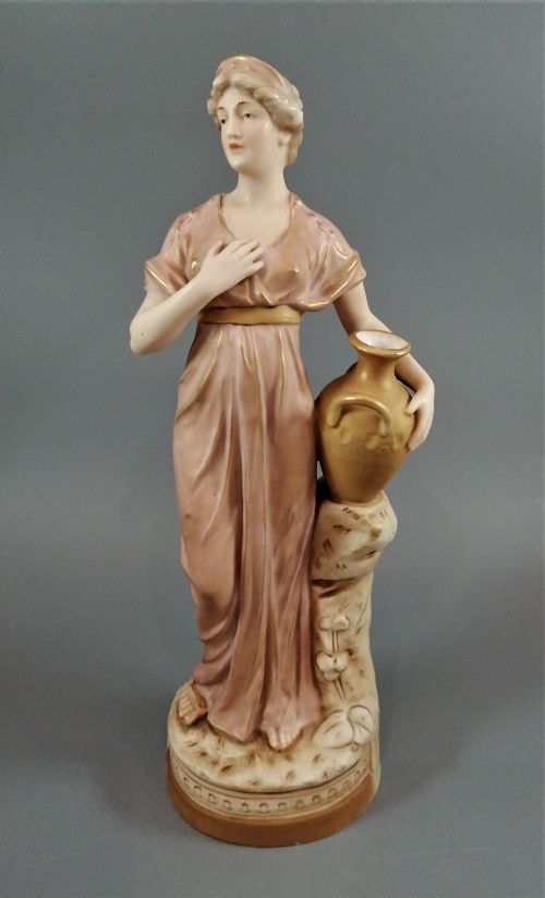 fig 1. An antique Royal Dux porcelain figurine depicting a woman in a draped pink gown holding a gilded water jug.