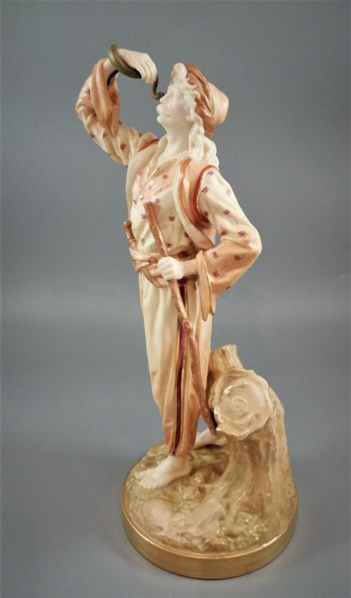 fig 1. A nineteenth-century Royal Worcester porcelain figurine depicting a standing snake charmer holding a snake aloft beside a tree stump base.