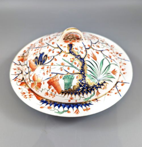 fig 1. A circular antique porcelain butter dish with stand, decorated with hand-painted Japanese Kakiemon style quail and floral motifs in iron-red, blue, and gold.