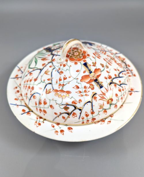 fig 3. A circular antique porcelain butter dish with stand, decorated with hand-painted Japanese Kakiemon style quail and floral motifs in iron-red, blue, and gold.