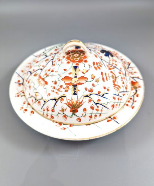 fig 4. A circular antique porcelain butter dish with stand, decorated with hand-painted Japanese Kakiemon style quail and floral motifs in iron-red, blue, and gold.
