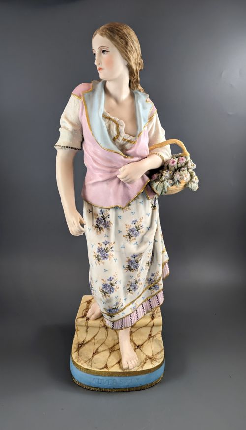 fig 1. A Victorian coloured Parian porcelain figure depicting a draped female figure holding a basket of flowers on a faux-marble painted base.