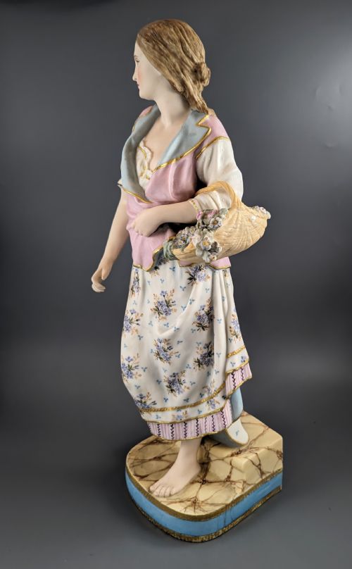 fig 3. A Victorian coloured Parian porcelain figure depicting a draped female figure holding a basket of flowers on a faux-marble painted base.