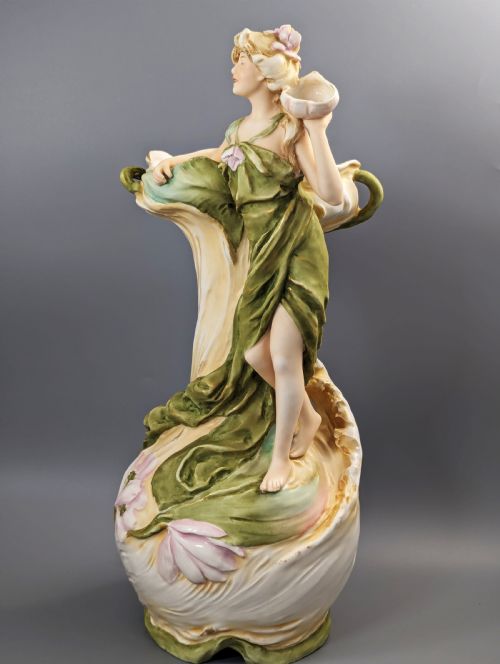 fig 1. An Art Nouveau Royal Dux porcelain vase depicting a draped water nymph holding a seashell against flowing foliage in cream, olive green, and soft pink shades.