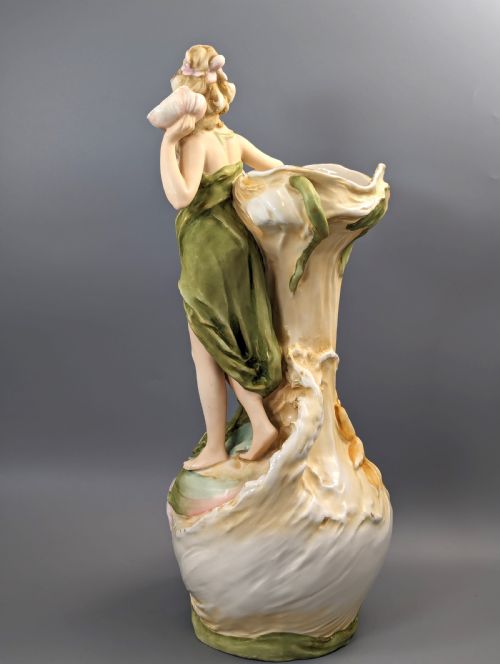 fig 2. An Art Nouveau Royal Dux porcelain vase depicting a draped water nymph holding a seashell against flowing foliage in cream, olive green, and soft pink shades.