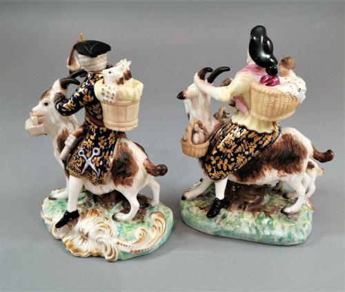 fig 2. A pair of painted porcelain figurines depicting a man and woman in 18th-century attire riding goats with cobalt blue gilded jackets on rococo scroll bases.