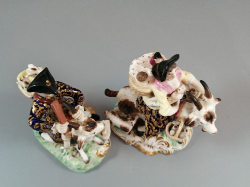 fig 5. A pair of painted porcelain figurines depicting a man and woman in 18th-century attire riding goats with cobalt blue gilded jackets on rococo scroll bases.