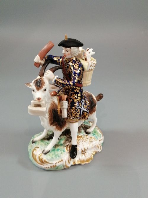 fig 6. A pair of painted porcelain figurines depicting a man and woman in 18th-century attire riding goats with cobalt blue gilded jackets on rococo scroll bases.