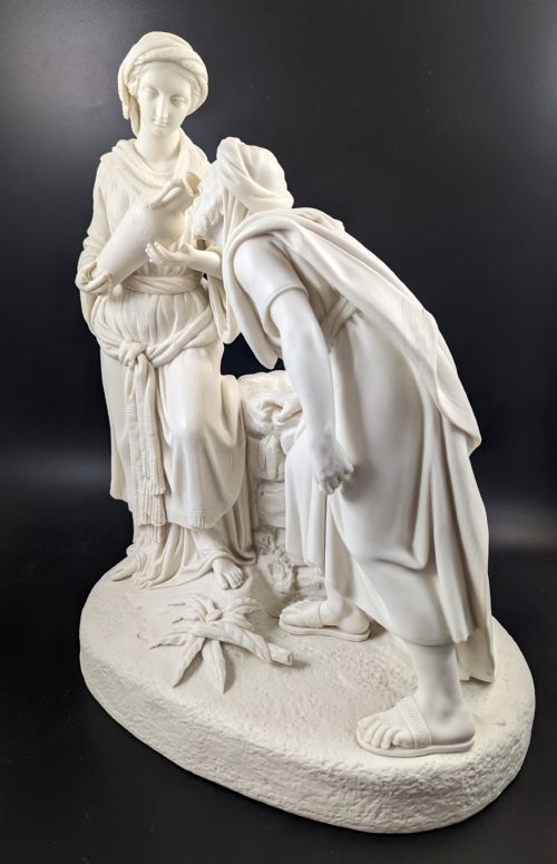 fig 1. An off-white Parian porcelain sculpture depicting Rebekah offering water from an amphora to a kneeling man beside a textured stone well.