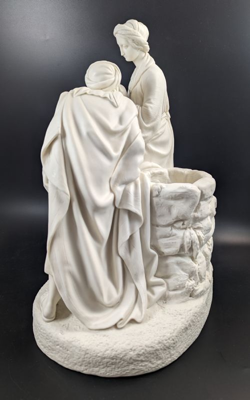 fig 2. An off-white Parian porcelain sculpture depicting Rebekah offering water from an amphora to a kneeling man beside a textured stone well.