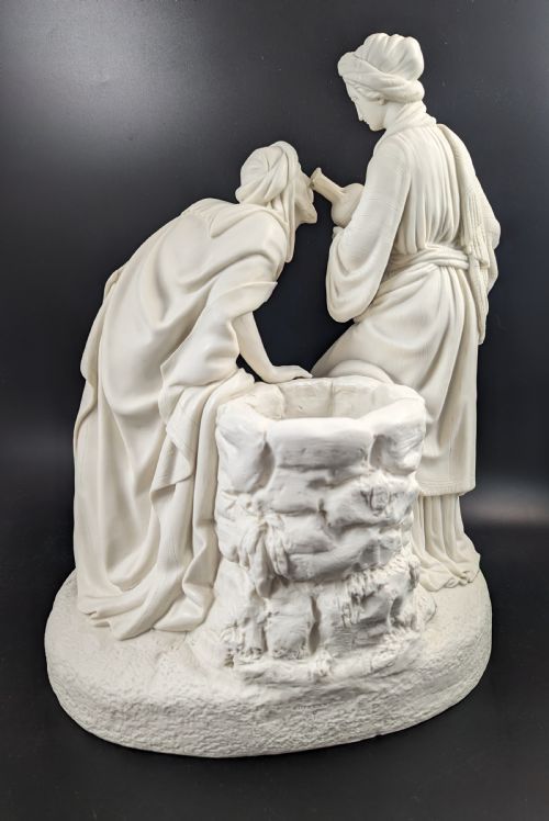 fig 3. An off-white Parian porcelain sculpture depicting Rebekah offering water from an amphora to a kneeling man beside a textured stone well.