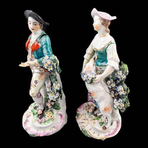 fig 3. A pair of eighteenth-century Derby soft-paste porcelain figurines depicting a shepherd and shepherdess adorned in floral-patterned garments with garlands on scroll bases.
