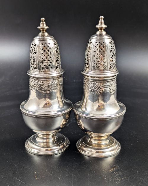 fig 1. A pair of George II sterling silver baluster-form casters featuring pierced lattice tops, chased scroll detailing, and stepped pedestal bases.
