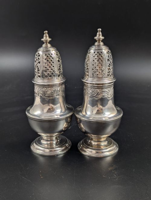 fig 2. A pair of George II sterling silver baluster-form casters featuring pierced lattice tops, chased scroll detailing, and stepped pedestal bases.
