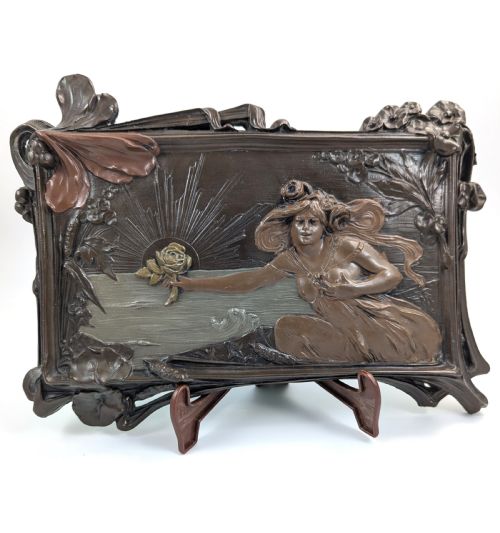 fig 1. A rectangular French Art Nouveau terracotta relief featuring a draped female figure holding a rose against a rising sun background with a metallic finish.