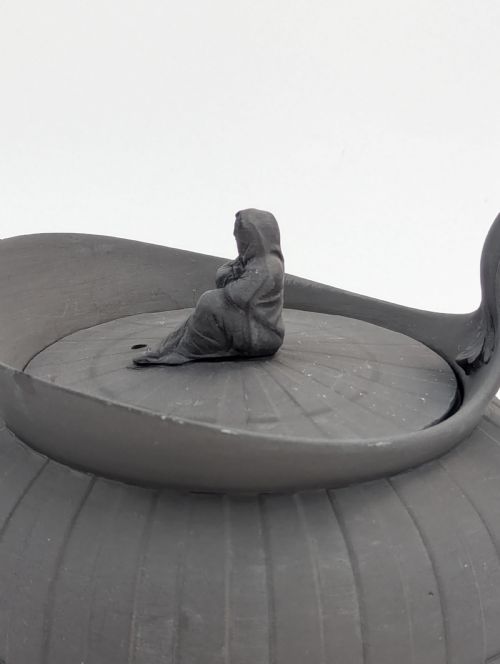 fig 1. An eighteenth-century Wedgwood black basalt teapot featuring a ribbed stoneware body, high loop handle, and a seated female figure finial on the lid.
