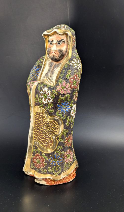 fig 1. A Japanese Satsuma earthenware figurine depicting a bearded Daruma monk wearing a hooded robe with polychrome enamels and gold accents.