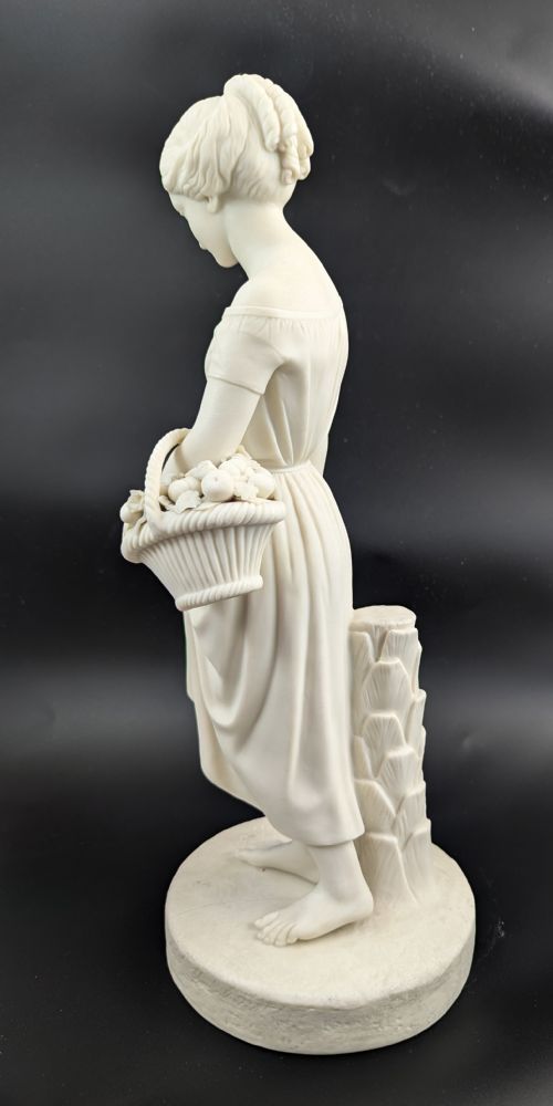 fig 2. An off-white Parian porcelain figurine depicting a standing classical female figure holding a fruit basket on a circular base.