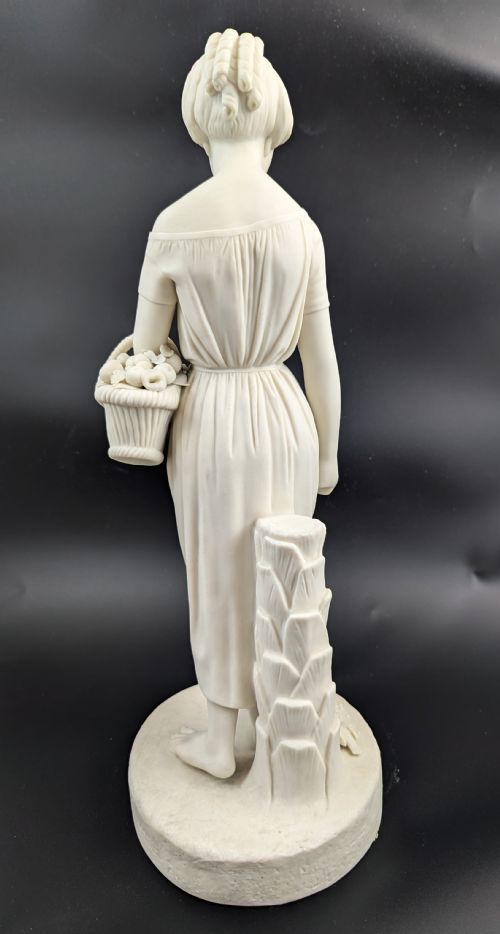 fig 4. An off-white Parian porcelain figurine depicting a standing classical female figure holding a fruit basket on a circular base.