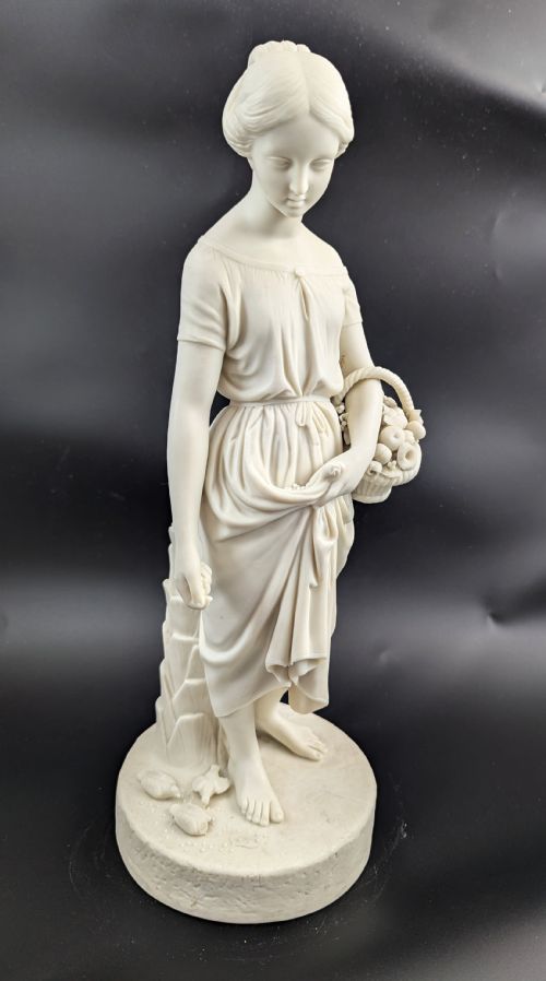fig 6. An off-white Parian porcelain figurine depicting a standing classical female figure holding a fruit basket on a circular base.