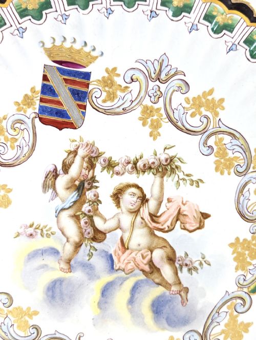 fig 3. A pair of 18th-century French tin-glazed earthenware display plates with hand-painted putti motifs, armorial shields, and green scalloped borders.