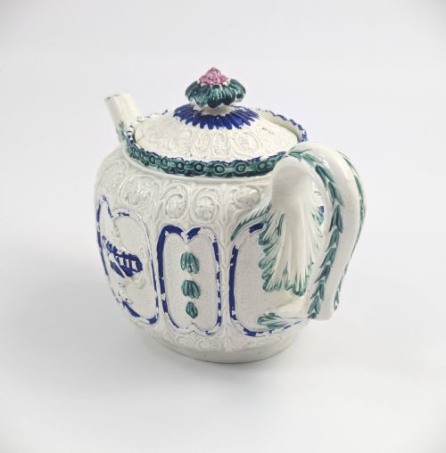 fig 1. An 18th-century lead-glazed ceramic teapot featuring relief-moulded arches, blue and green painted accents, and a moulded lid with a pink flower finial.