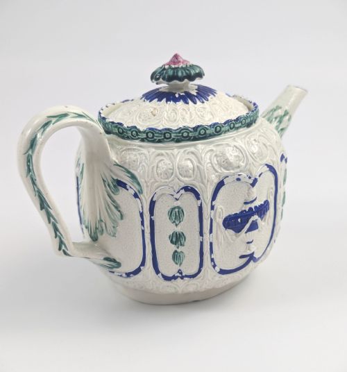 fig 2. An 18th-century lead-glazed ceramic teapot featuring relief-moulded arches, blue and green painted accents, and a moulded lid with a pink flower finial.
