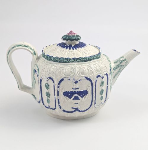 fig 3. An 18th-century lead-glazed ceramic teapot featuring relief-moulded arches, blue and green painted accents, and a moulded lid with a pink flower finial.