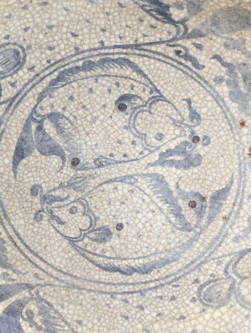 fig 1. A circular antique ceramic dish featuring a central underglaze grey fish design on a crazed cream ground.
