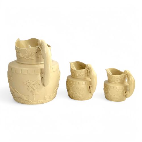 fig 2. A graduated set of three buff yellow Regency ceramic pitchers featuring relief-moulded stag hunting scenes and sculpted hound handles.