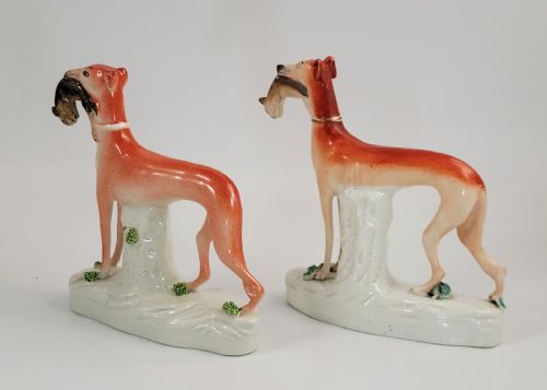 fig 1. A pair of Victorian Staffordshire earthenware greyhound figurines standing on white bases with caught hares held in their mouths.