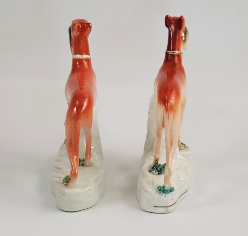 fig 2. A pair of Victorian Staffordshire earthenware greyhound figurines standing on white bases with caught hares held in their mouths.