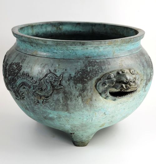 fig 1. A tripod Chinese bronze censer decorated with raised dragon motifs, mask handles, and a verdigris surface finish.