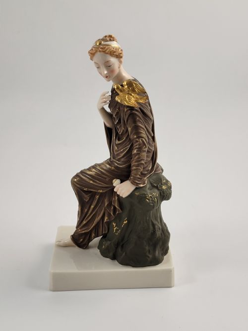 fig 1. A Victorian Royal Worcester porcelain figurine depicting a seated classical maiden in a draped brown robe decorated with gold accents, with a gilded dove on her shoulder.