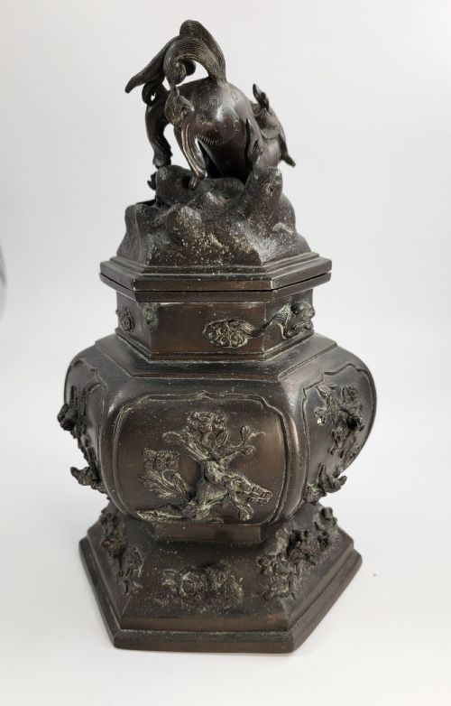 fig 1. A dark patinated hexagonal bronze incense burner featuring floral relief panels and topped with a sculpted Fu lion finial.